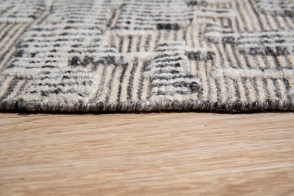 The high-texture gray and cream geometric patterned rug rests on light blonde hardwood flooring.