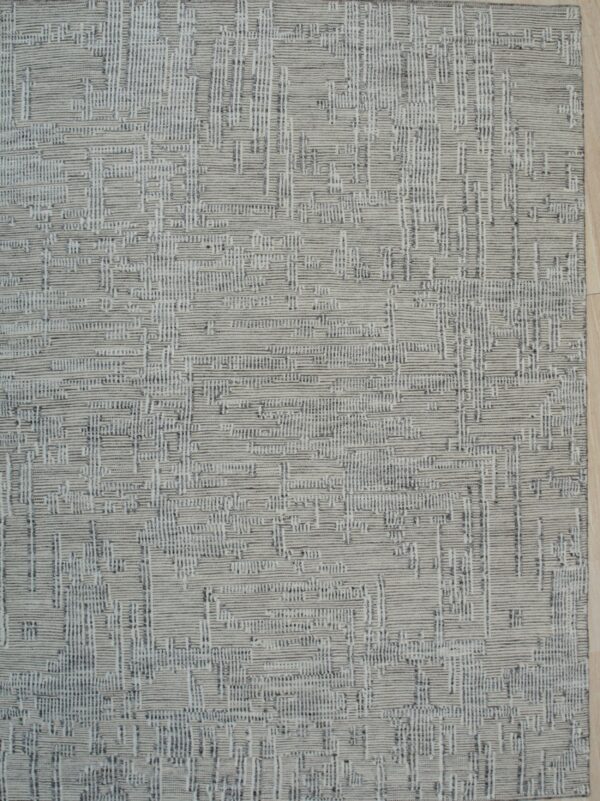 Textured gray rug displaying a dense linear geometric pattern, placed on light wood plank flooring.
