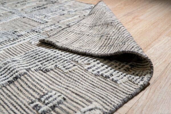 Textured gray and cream rug with a geometric grid pattern is folded on light wooden floor.