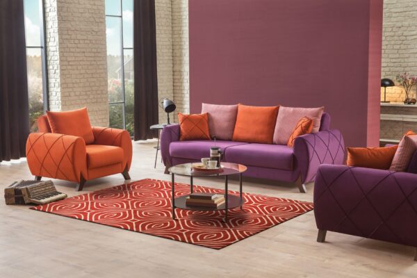 A red and cream geometric rug anchors a purple sofa and orange armchairs on a light wood floor.