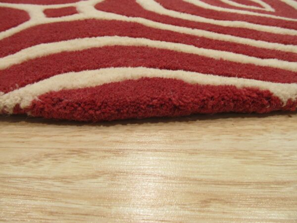 Close-up of a high-pile rug featuring thick red and cream wavy stripes on a glossy light wood floor.