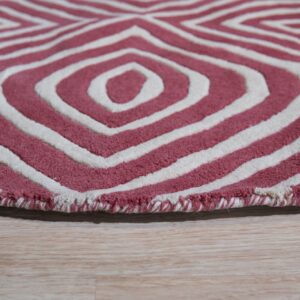 A deep pink and cream rug with carved concentric diamond patterns rests on light wood planks.