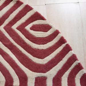 Textured maroon and cream rug displaying a bold interlocking geometric design on blonde wood flooring.