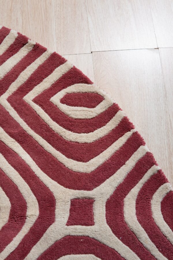 Textured maroon and cream rug displaying a bold interlocking geometric design on blonde wood flooring.