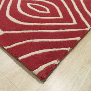 Close-up of a red area rug with thick cream abstract lines resting on light wood flooring.