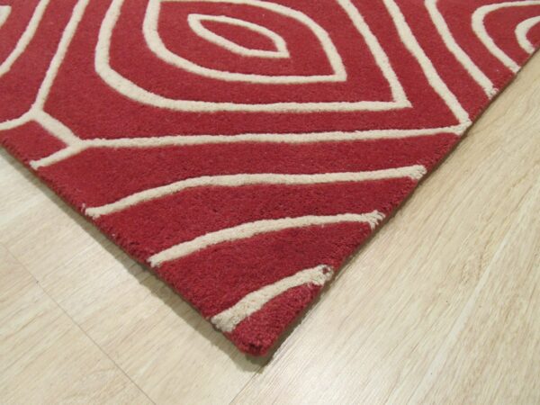 Close-up of a red area rug with thick cream abstract lines resting on light wood flooring.
