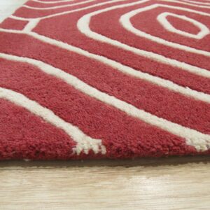 Thick-pile red and white rug with a bold geometric curve pattern rests on light wood planks.
