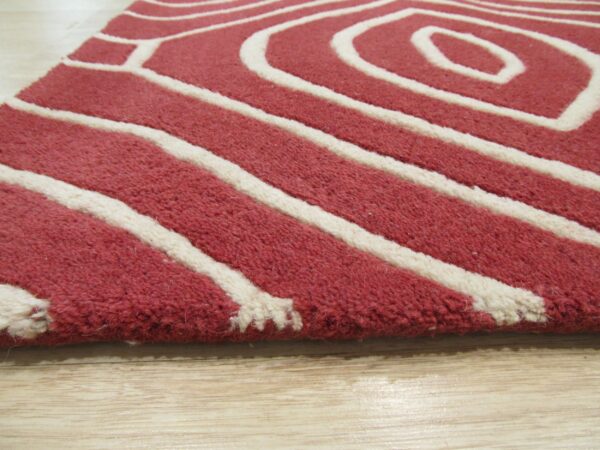 Thick-pile red and white rug with a bold geometric curve pattern rests on light wood planks.