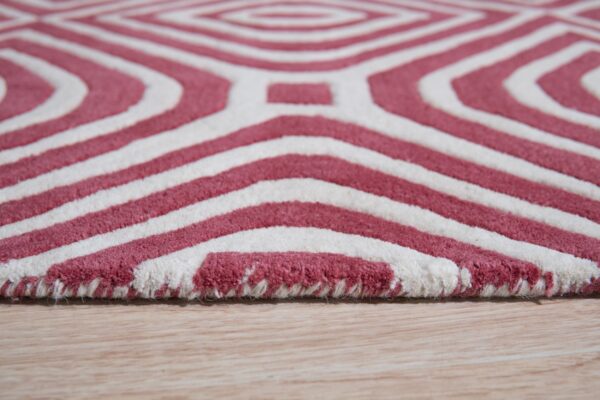 A thick, rose red and white rug featuring a geometric diamond pattern on light wood flooring.