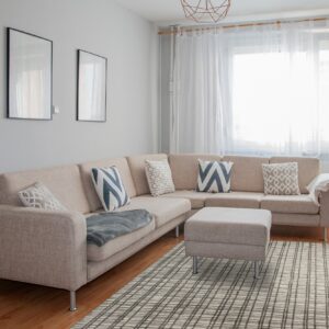 Gray and beige grid pattern rug partially under a large light-colored sectional sofa on hardwood floor.
