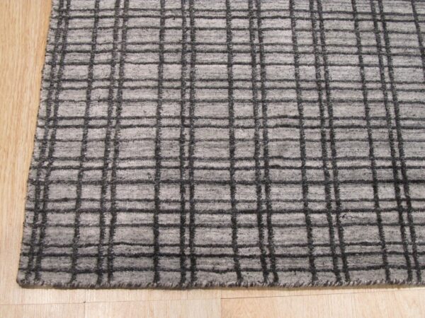 Textured light gray rug featuring a dark grid pattern placed on light colored wood flooring.