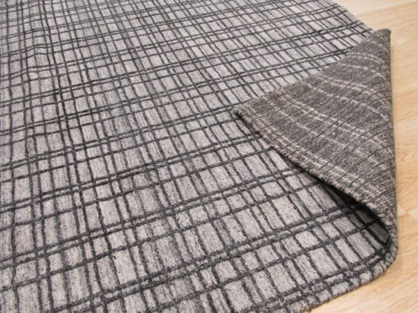 Light gray plaid rug folded over, revealing a dark heathered woven backing on a wood floor.