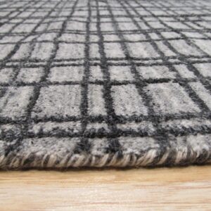 Close-up of a fuzzy gray rug with a dark charcoal plaid pattern over light wood.
