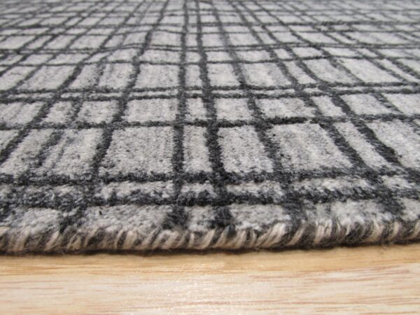 Close-up of a fuzzy gray rug with a dark charcoal plaid pattern over light wood.