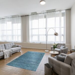 A teal-blue textured rug sits between gray upholstered furniture on herringbone wood flooring.