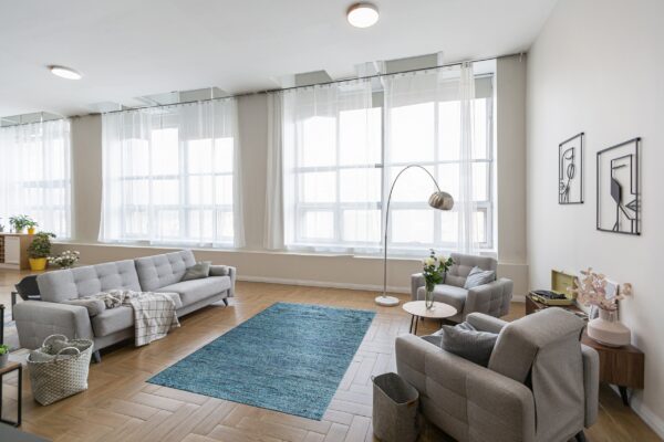 A teal-blue textured rug sits between gray upholstered furniture on herringbone wood flooring.
