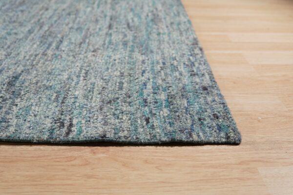 Thick pile rug in shades of blue, teal, and gray resting on light hardwood floors.