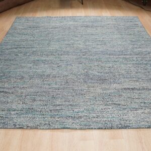 Light blue and gray variegated textured rug lying flat on blonde wooden plank flooring.