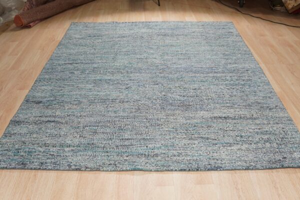 Light blue and gray variegated textured rug lying flat on blonde wooden plank flooring.