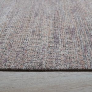 Close-up showing the soft, textured pile of a beige and purple abstract rug resting on light wood floors.