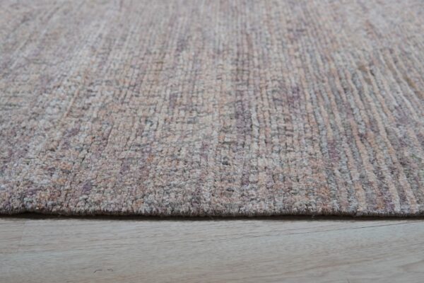 Close-up showing the soft, textured pile of a beige and purple abstract rug resting on light wood floors.