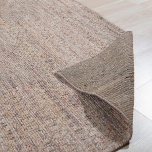 Low pile, mottled beige rug with the corner flipped to show the dark backing on a light wood floor.