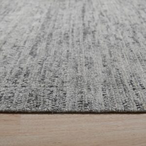 Low-angle view of a thick, mottled gray and charcoal rug resting on light wood flooring.