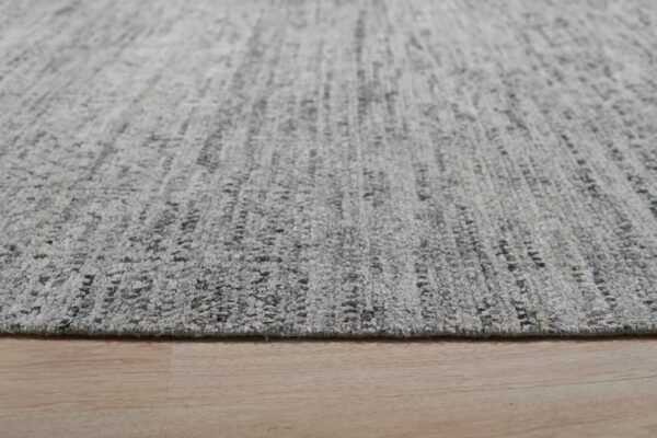 Low-angle view of a thick, mottled gray and charcoal rug resting on light wood flooring.