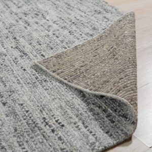 Speckled gray textured rug pile and woven tan backing displayed on light wood floorboards.