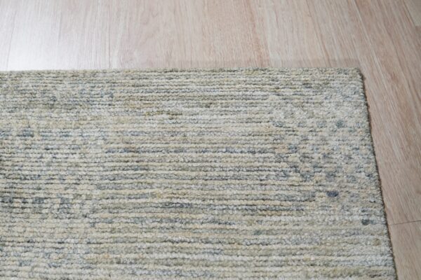 A beige and gray striated textured rug corner shown on light blonde wood flooring.