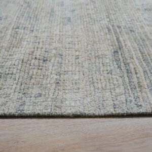 A textured, high-pile beige rug with blue speckles rests on light colored plank wood flooring.