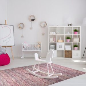 A low-pile, multicolored pink and dark-toned rug anchors a bright white nursery with a rocking horse.