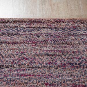 Textured rug edge in mottled pink, navy, and beige fibers against light wood flooring.