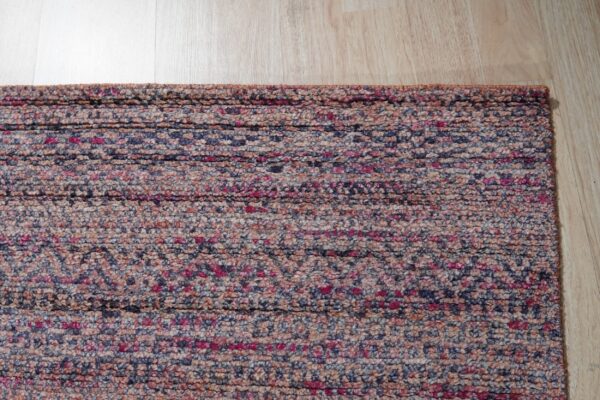 Textured rug edge in mottled pink, navy, and beige fibers against light wood flooring.