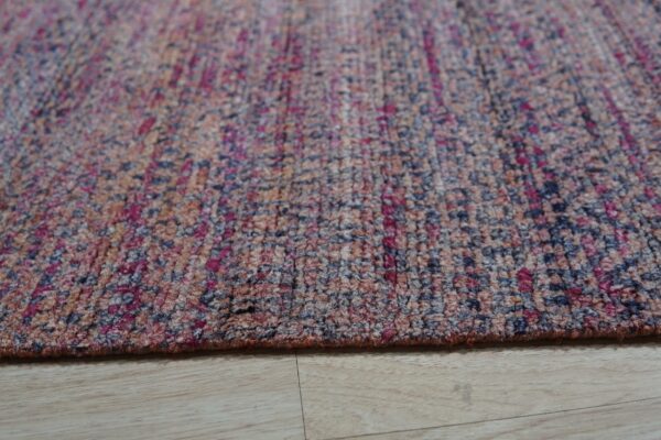 Close-up of a flecked rug in magenta, navy, and earth tones resting on light wood plank flooring.