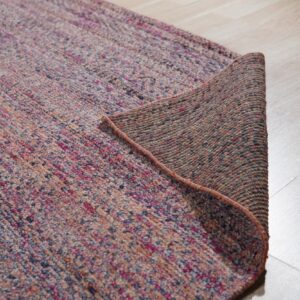 Flecked magenta, purple, and beige rug corner is lifted, revealing the dark woven backing.