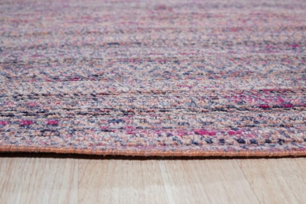 Speckled pink, blue, and beige low-pile rug with a textured weave rests on light wood planks.