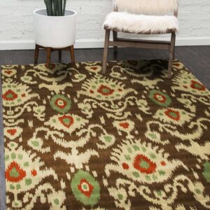 A brown, beige, green, and rust ikat patterned rug rests on dark wood flooring beside a furry white chair and a potted snake plant.