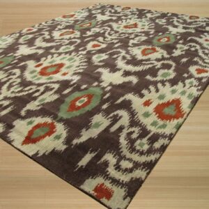 Dark brown rug with cream, rust, and green abstract ikat pattern lying on light wood flooring.