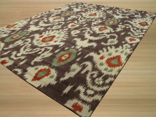 Dark brown rug with cream, rust, and green abstract ikat pattern lying on light wood flooring.