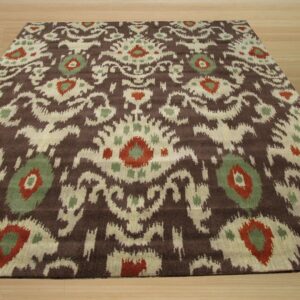 Angled view of a low pile rug featuring a brown, cream, red, and sage ikat pattern on light wood flooring.