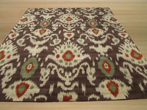 Angled view of a low pile rug featuring a brown, cream, red, and sage ikat pattern on light wood flooring.