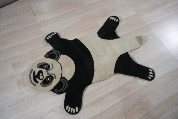 A shaped black, cream, and gray panda rug rests on light wood-look flooring.