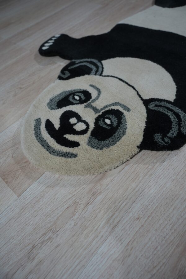 A black, cream, and gray panda-shaped rug rests on light wood plank flooring.