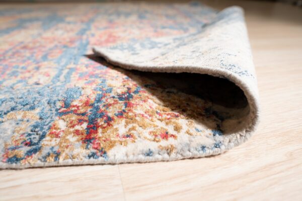 A distressed blue, red, and gold patterned rug is rolled back on a light wood plank floor.