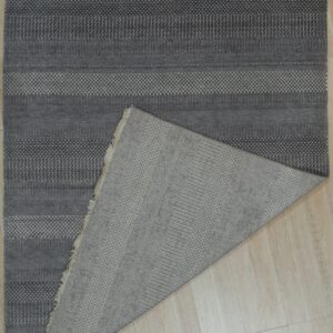 Dark gray textured rug with geometric stripes is folded over on light wood flooring.