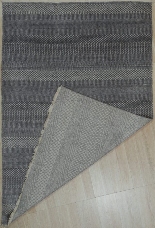 Dark gray textured rug with geometric stripes is folded over on light wood flooring.