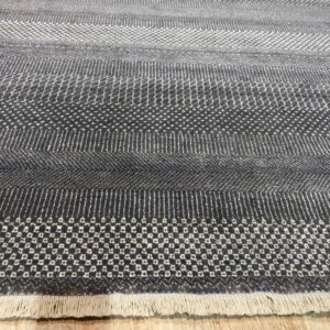 Geometric gray rug with varying textured horizontal stripes and small fringe resting on wood floor.
