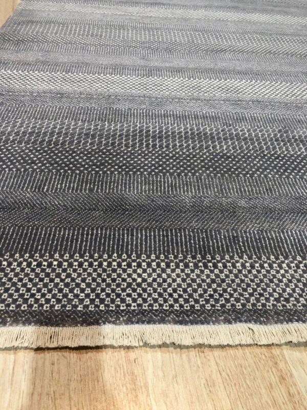 Geometric gray rug with varying textured horizontal stripes and small fringe resting on wood floor.