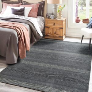 Dark gray rug with light patterned horizontal stripes under a bed on gray wood floors.